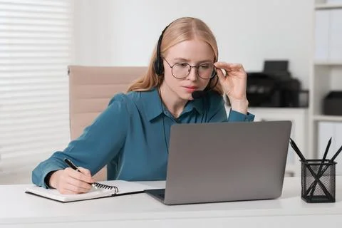 Interpreter in headset taking notes while working with laptop at table indoor Stock Photos