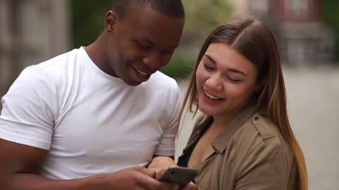 Interracial couple having fun with smartphone in the city street. Young Stock Footage 132738049
