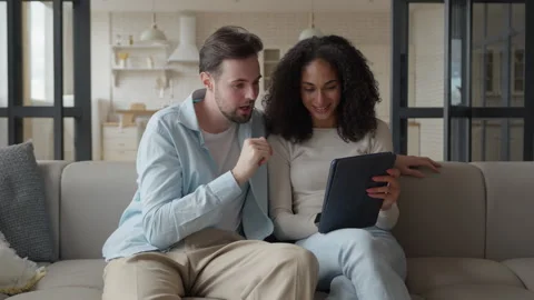 Interracial Couple Laughing While Browsing Tablet And Receiving Good News Stock Footage 303085196