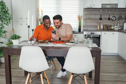 Interracial couple looking at smartphone while having breakfast in the kitchen Stock Photos