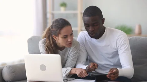 Interracial couple using calculator calculating paying domestic bills on laptop Stock Footage 108121394