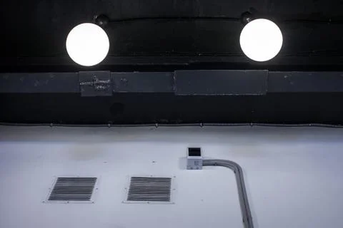Interrior fragment of black ceiling with two lamps and white wall with bars Stock Photos