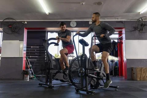 Interval timer beeping, two men gripping fan bike handles and pedaling hard for Stock-Fotos