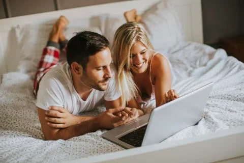 Intimate lovers using laptop lying on the bed Stock Photos