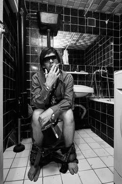 Intoxicated Man Smoking Cigarette While Sitting on Toilet Stock Photos