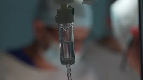 Intravenous drip in operation room with surgeons on background Stock Footage 147181750