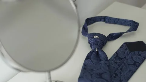 Intricate blue tie with paisley patterns and a silver pin, lying on a white Stock Footage 295098693