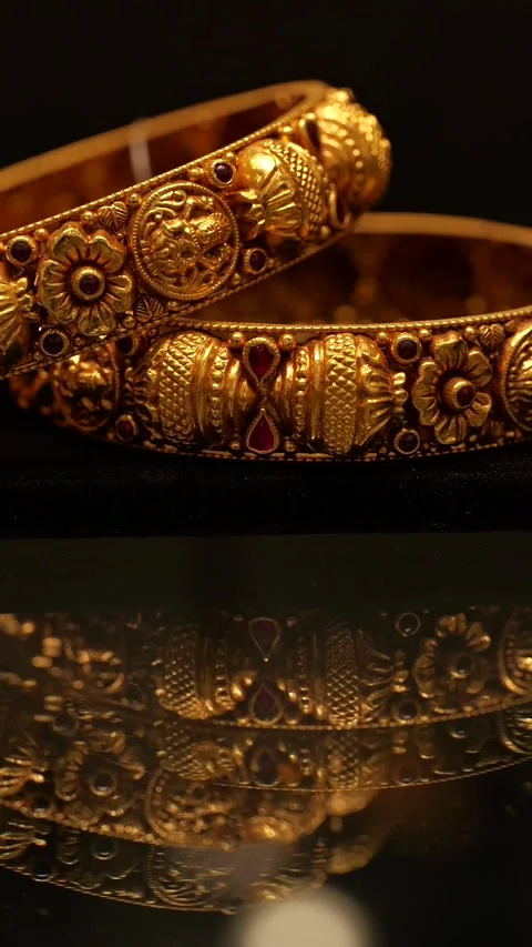 Intricate gold bangles with red gemstone accents displaying ornate metal texture Stock Footage 346248564