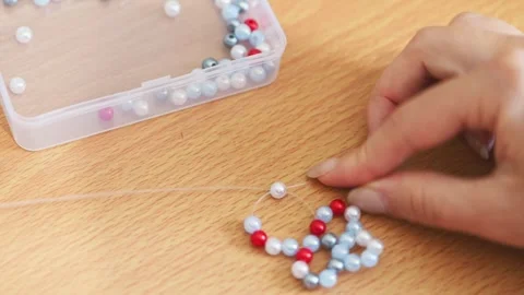 Intricate handmade beadwork assembling with vibrant red and pearl beads on .. Stock Footage 339566532