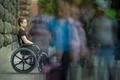 The invalid man sit in the wheel chair in the crowd stream at sidewalk Photo