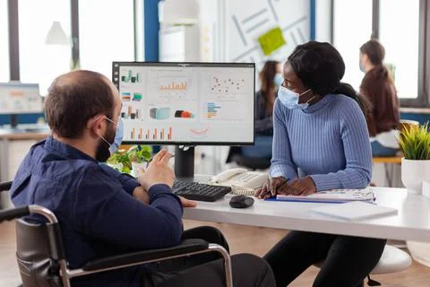 Invalid manager with face mask explaning to black employee financial evolution Foto stock