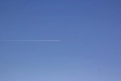 Inversion trail of clouds from the plane against the blue sky. Airplane leaving Stock Photos
