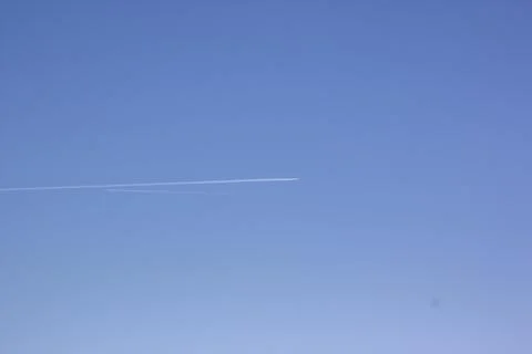 Inversion trail of clouds from the plane against the blue sky. Airplane leaving Stock Photos