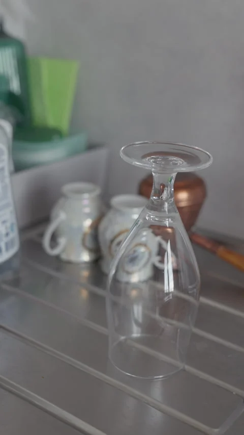 Inverted wine glass drying on kitchen counter with blurred ceramic cups and Stock Footage 344823909