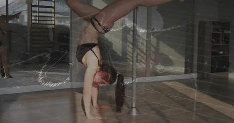 Inverting dancer moving on metal pole in studio with mirrors, wearing black Stock Photos