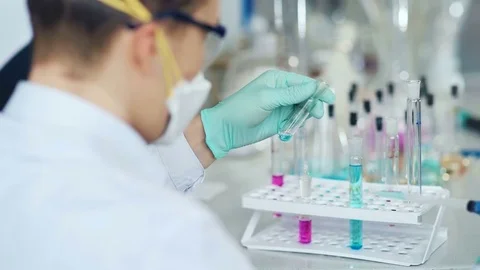 Investigator checking test tubes. Man wears protective goggles and mask Stock Footage 85328905