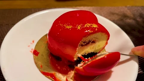 An invisible hand with a fork breaks off a piece of heart-shaped mousse cake Stock Footage 240546760