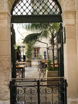 An inviting inner courtyard with palm trees is accessible through an iron gate, Fotos de archivo