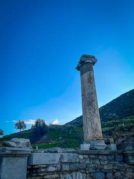 Ionic Column Soars Above Rubble-Strewn Hillside Under Azure Sky Fotos de archivo