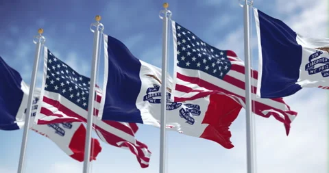 Iowa state flags waving in the wind with the US flags on a clear day Stock Footage 318109870