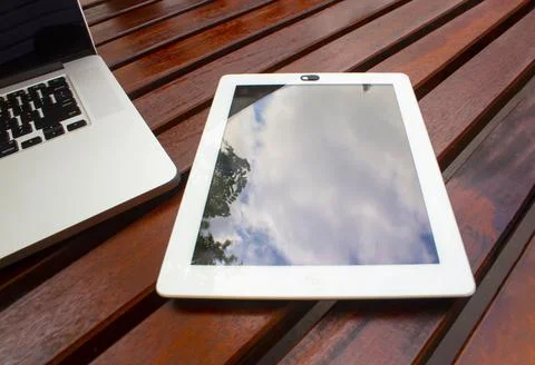 An iPad on a wooden table next to a computer 스톡 사진