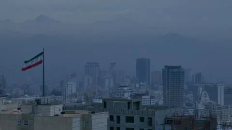 Iranian flag over Tehran skyline with misty mountains in the background Stock Footage 317836644