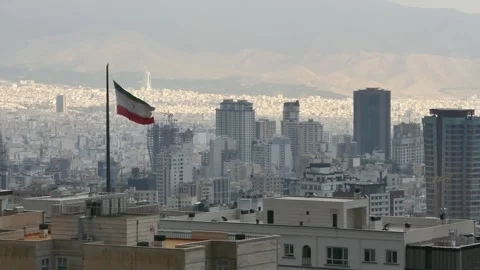 The Iranian flag waves on a tall pole above Tehran skyline Stock Footage 318922306