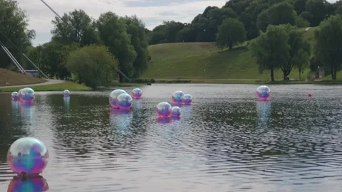 Iridescent Balls Floating on Calm Park Lake, Green Hill Behind, Wide Shot Stock-Footage 343022951