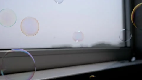 Iridescent Bubbles Drift and Pop Near a Window Sill Stock Footage 316179509