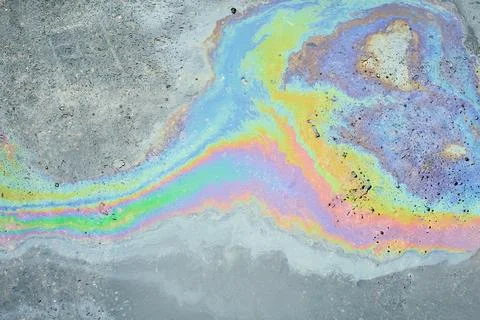 Iridescent fluid creating an abstract rainbow pattern on wet pavement, showing Stockfoto's