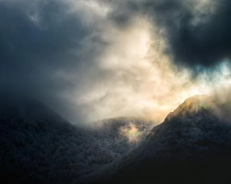 Iridescent phenomenon in the clouds between snow capped peaks Фото
