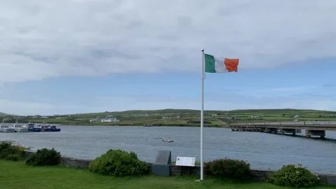 Irish flag on a big white pole is waiving from a heavy wind. Portmagee, Ireland Stock Footage 247549359