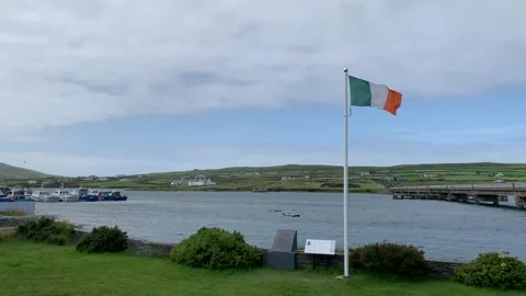 Irish flag on a big white pole is waiving from a heavy wind. Portmagee, Ireland Stock Footage 247549584