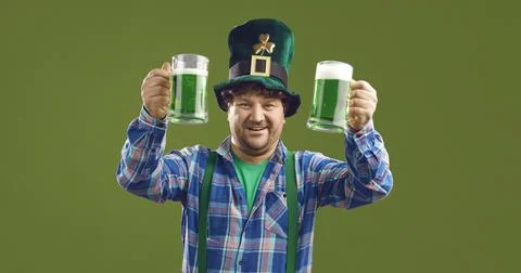 Irish man in Patrick hat with two raised beers isolated on green copy space Stock-Fotos