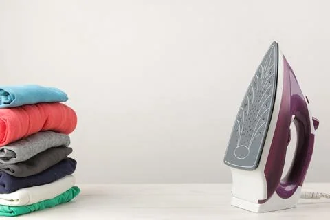 Iron and a stack of colored clothes on a white background. Ironing of clothes Stock Photos