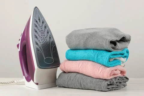 Iron and a stack of colored clothes on a white background. Ironing of clothes Stock Photos