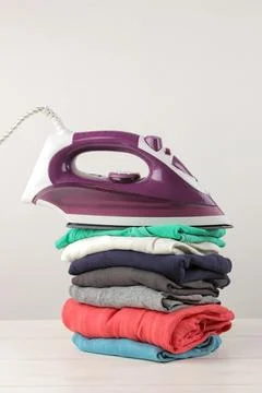 Iron and a stack of colored clothes on a white background. Ironing of clothes Stock Photos