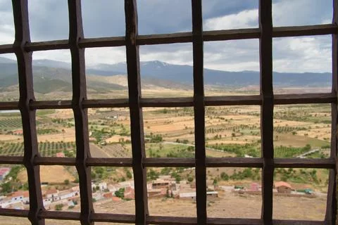 Iron bars frame a vast, sunlit valley 库存照片