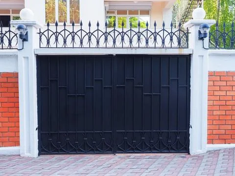 Iron black gate with a wrought pattern and sharp tips at the top and with a Stock Photos