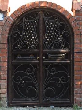 Iron dark gate with a gilded pattern next to a brick fence with an arch. Private Stock Photos