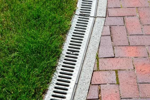 Iron drainage system between paving slabs and green lawn. Stock Photos
