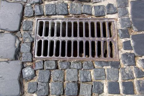 The iron grate of the drainage system hatch on the road paved. Stock Photos