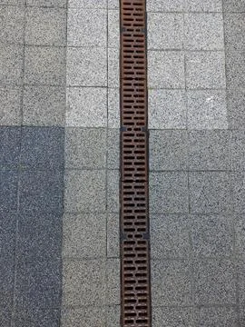 Iron grating on the drainage gutter on the tiled pavement for water drainage Foto stock