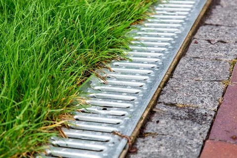 An iron gutter with grate to the drainage system on the side of footpath. Stock Photos