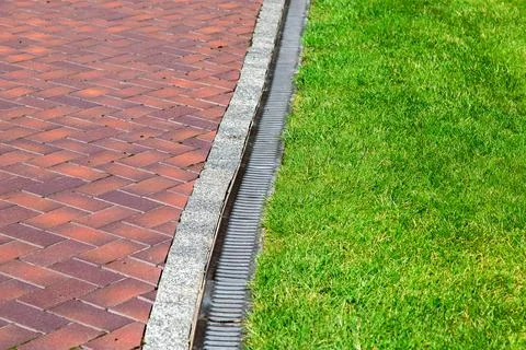 Iron gutter with grate to the drainage system on the side of the footpath. Stock Photos