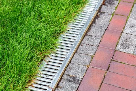 An iron gutter with grate to the drainage system on the side of footpath. Stock Photos