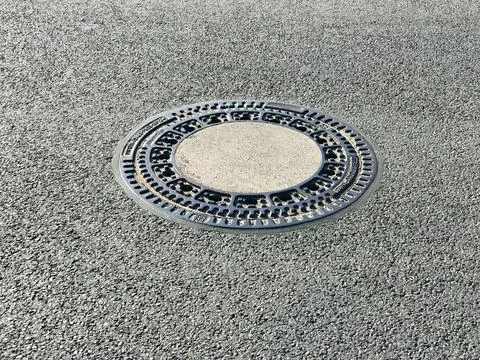 Iron hatch with a pattern above an observation well is located on auto road in Stock Photos