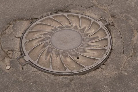 A iron hatch with a pattern above an observation well is located on auto road in Stock Photos