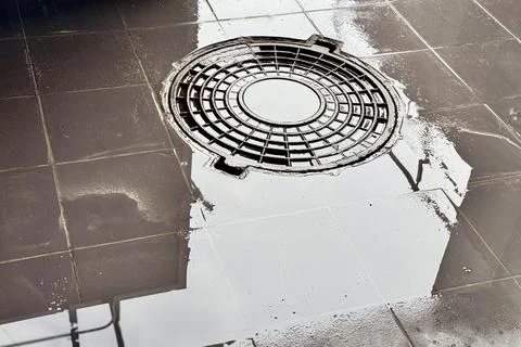 A iron hatch with a pattern and covered water above an observation well is Stock Photos