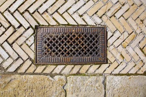 Iron rusty rectangular manhole with shaped holes in the lid on the sidewalk. Stock Photos